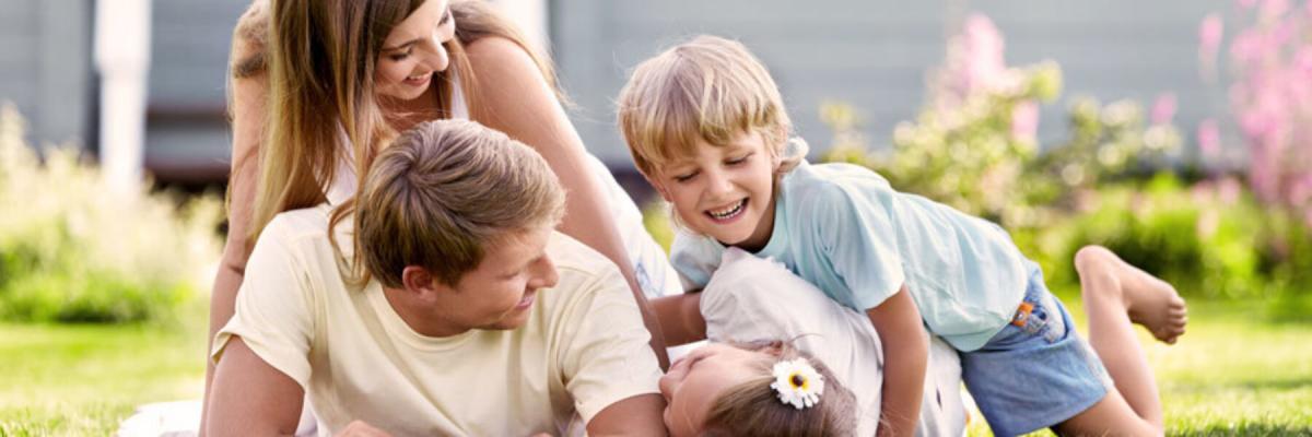 Happy family of man, woman, and two children rolling and playing on the grass, Family Doctor